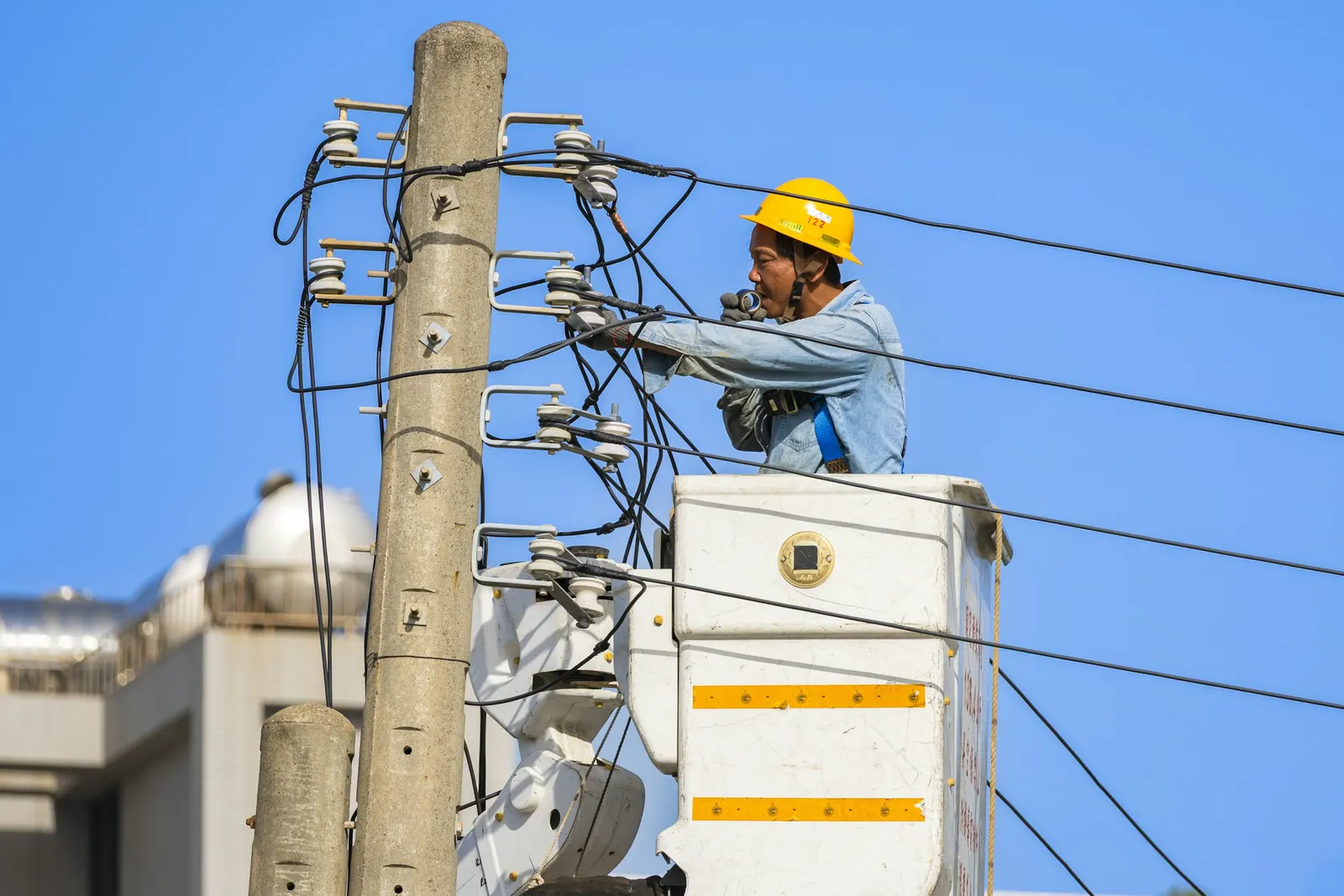 Line technician in a bucket lift working on a wooden pole's crossarms