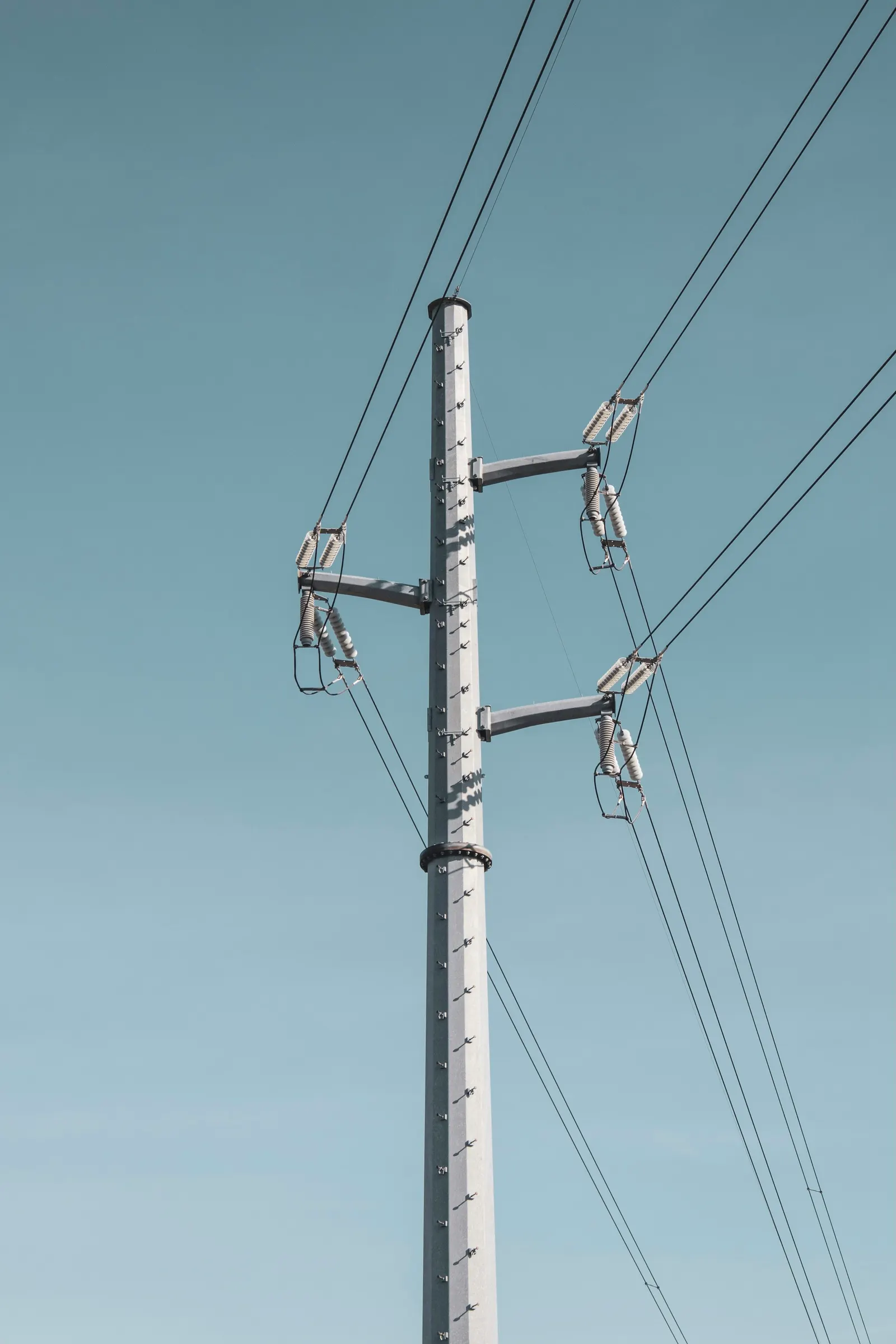 Single concrete pole carrying a few cleanly tensioned lines against a pale sky
